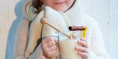 a woman holding a glass of milk with a straw in her hand while wearing a scarf