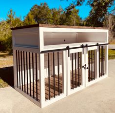 a dog kennel with doors and railings on the side of a road in front of some trees