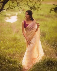 a woman in a sari standing under a tree with her hands on her hips