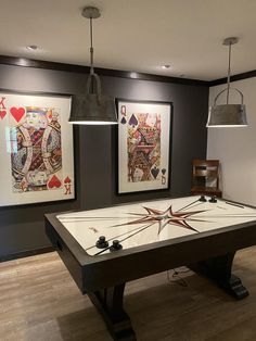 a pool table in a room with two pictures on the wall and one light hanging over it