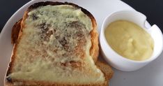 a white plate topped with two slices of bread and cheese next to a bowl of mustard