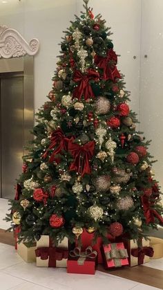 a christmas tree decorated with red and silver balls, ornaments and bows is in the lobby