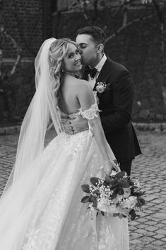 black and white photo of bride and groom kissing each other on the cobblestone