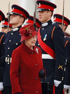 the queen and prince are standing next to each other wearing red coats with matching hats