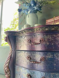 an ornately painted chest of drawers with flowers in the background