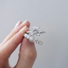 a woman's hand holding an engagement ring with three stones on it and two fingers