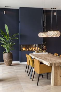 a modern dining room with blue walls and wooden table surrounded by yellow chairs in front of a fireplace