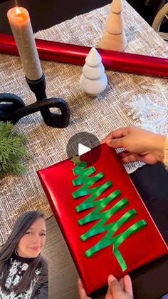 a woman is making a christmas tree out of construction paper and glue on a piece of red cardboard