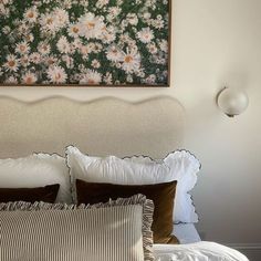 a bed with white and brown pillows in a bedroom next to a painting on the wall