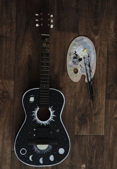 a guitar and paintbrush on a wooden floor