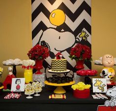 the dessert table is decorated with red and yellow flowers, peanutshells, chevron paper napkins, candy bar wrappers, and snoopy treats