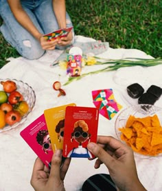 a person sitting on the ground holding up cards with food in front of them and other items