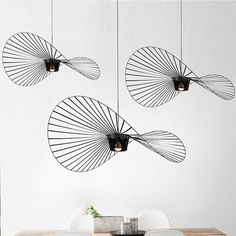 three hanging lights over a wooden table in front of a wall with white walls and chairs