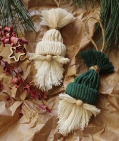 three knitted christmas ornaments sitting on top of a piece of brown paper next to pine branches