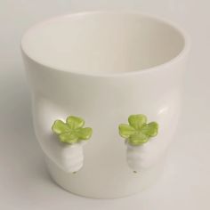 a white cup with two green flowers on the front and side, sitting on a table