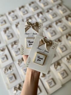 a person holding up two small white tags with bows on them, in front of a wall of framed pictures