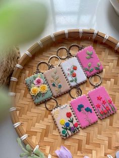 four embroidered keychains sitting on top of a bamboo tray next to some flowers