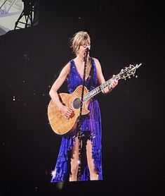 a woman in a blue dress holding a guitar and singing into a microphone on stage