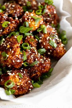 a white bowl filled with meat covered in sesame seeds and garnished with green leaves