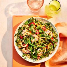 a salad with shrimp and spinach in a white bowl on an orange place mat