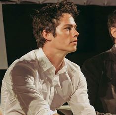 two men sitting next to each other in front of a microphone and one man wearing a white shirt