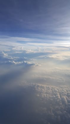 the view from an airplane window looking down on clouds and blue sky with sunbeams