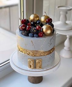 a white cake with gold decorations and berries on top is sitting on a window sill