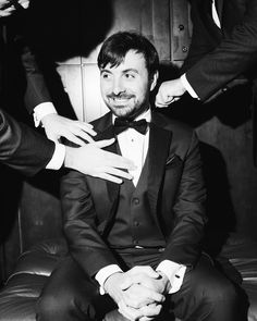 a man in a tuxedo smiles as he sits with two other men