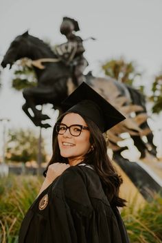 a woman wearing glasses and a graduation cap standing in front of a statue with a horse on it