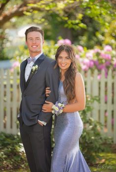 a man and woman in formal wear standing next to each other near a fence with flowers