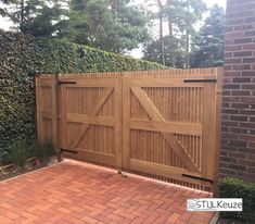 a wooden gate in the middle of a brick walkway next to a fence and shrubbery