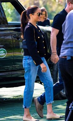 a woman in jeans and heels walking next to a black truck with people behind her