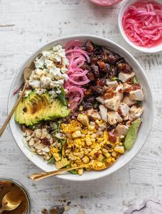 a bowl filled with chicken, avocado, onions and other foodstuffs