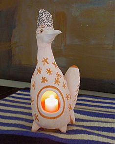 a ceramic bird with a lit candle in it's beak sits on a blue and white striped tablecloth