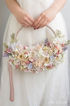 a woman wearing a white wedding dress holding a flowered basket in her hands,