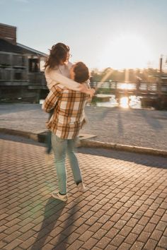 a man and woman are hugging on the sidewalk near water in the sun setting behind them