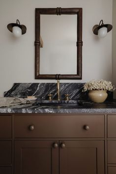 a bathroom vanity with marble counter top and gold faucet, along with two wall sconces