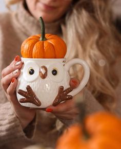 a woman holding a coffee cup with an owl on it and a pumpkin in the background