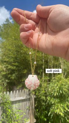 a hand holding a necklace with a small shell on it's chain and the words soft pink written in white