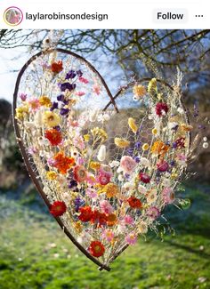 a heart shaped flower arrangement hanging from a tree in a field with grass and flowers