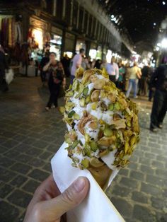 a hand holding up a pastry with toppings on it's head in front of a crowd of people