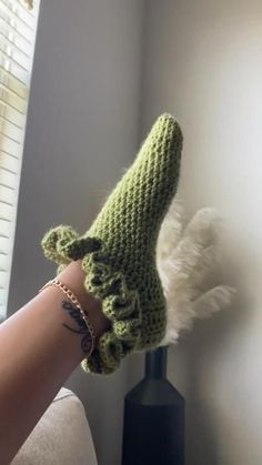 a woman's hand wearing a green crocheted slipper with white feathers