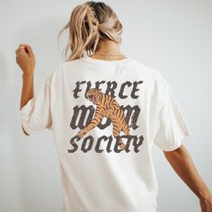 🐅Join the ranks of the fearless with our boho Fierce Mom Society Graphic Tee. Perfect for the edgy, strong, dynamic, and powerful women who shape the world, this shirt features a bold tiger graphic symbolizing strength and courage. Made for those who proudly lead their pack, it's more than just a shirt--it's a statement. The is the perfect oversized boho graphic tee for the mom you know and love! 🖤SHIRT MATERIAL Comfort Colors Unisex Shirt 100% Ring-Spun Cotton Printed using Direct To Garment style- Inks are printed directly into the fabric. Different sizing may effect placement of final design. Colors may differ slightly due to different user monitor and screen settings.  🏁SIZING Shirts are true-to-size for UNISEX RELAXED fit  Mockup photos are typically on sizes Medium & Large. Please Boho T-shirt, Cool Mom Shirts, Oversize Tshirt Outfits, Trending Graphic Tees, Tiger Graphic, Cool Mom, Badass Women, Mom Tees, Tshirt Outfits