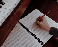 a person holding a pencil and writing on a sheet of paper with piano keys in the background