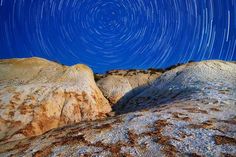 the night sky over some rocks with stars in the background and a star trail above them