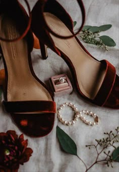 a pair of high heeled shoes sitting on top of a white blanket next to flowers