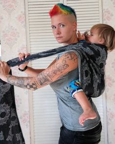 a woman carrying a baby in a sling with tattoos on her arm and shoulder,