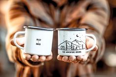 two people holding coffee mugs in their hands with mountains and stars painted on them