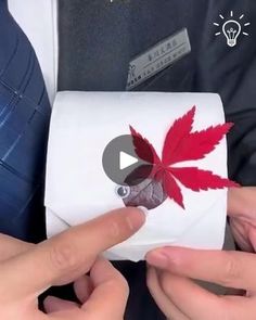 two hands holding a piece of paper with a red maple leaf on it, and another person's hand pointing at something