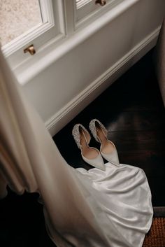 a bride's wedding dress and shoes sitting on the floor in front of a window